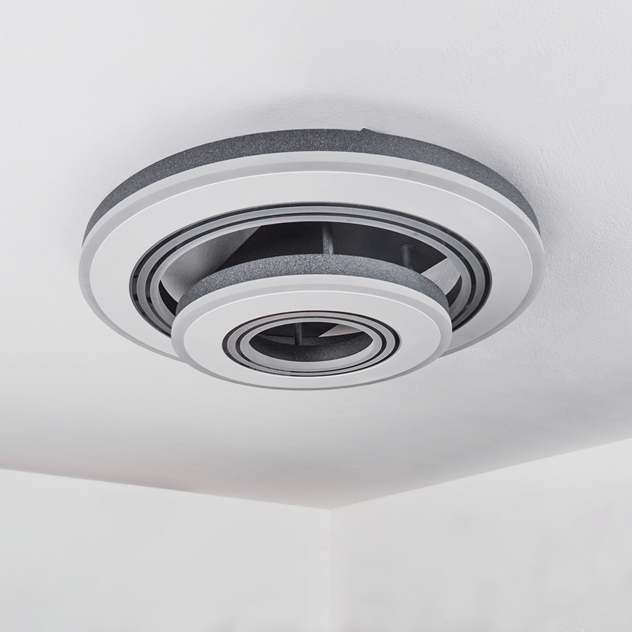 An der Decke montierte Leuchte. Sie hat ein kreisförmiges Design mit einem grauen Außenring und einem weißen Innenring.