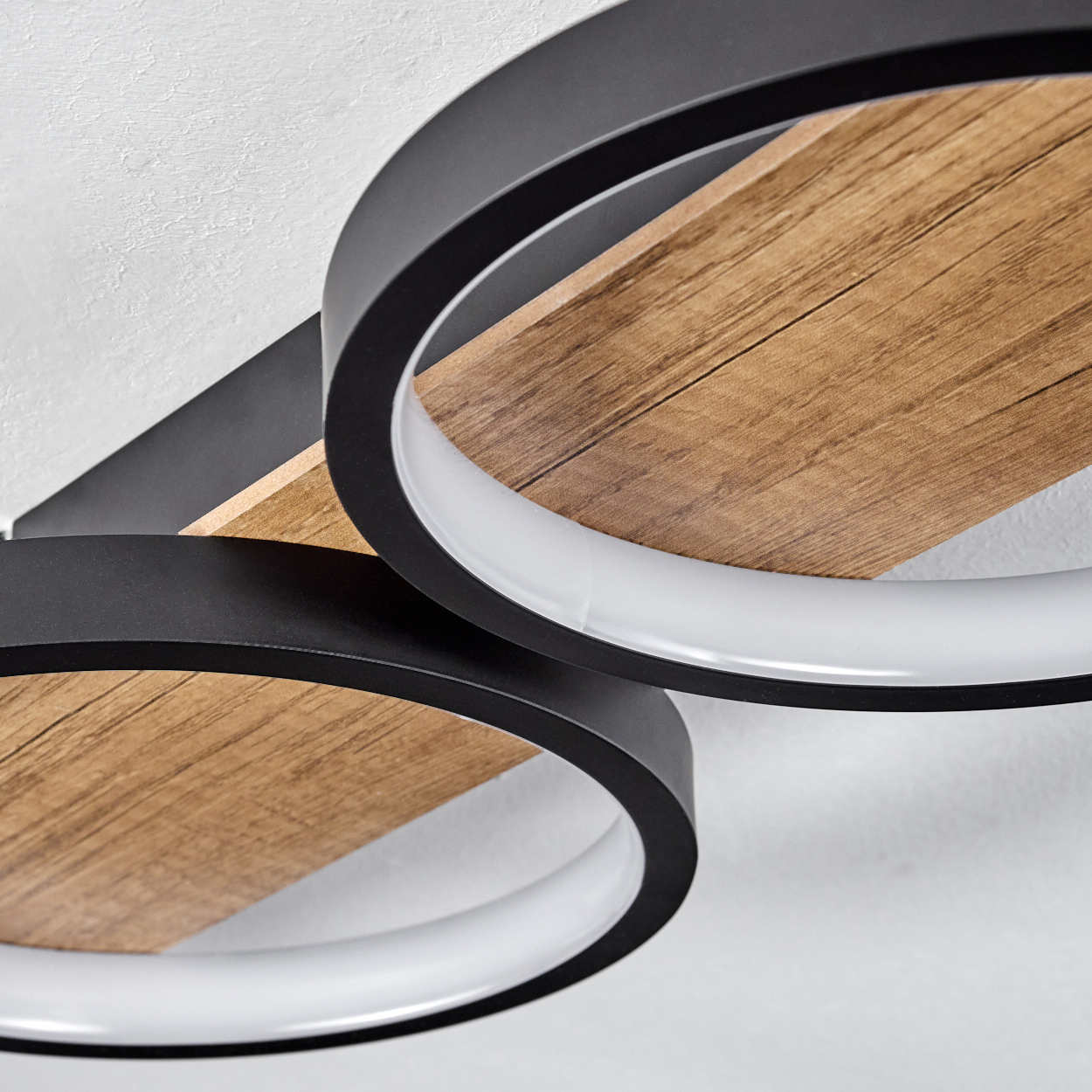Nahaufnahme einer Deckenleuchte mit Holzbalken und schwarzen Ringen mit weißem Innenlicht.