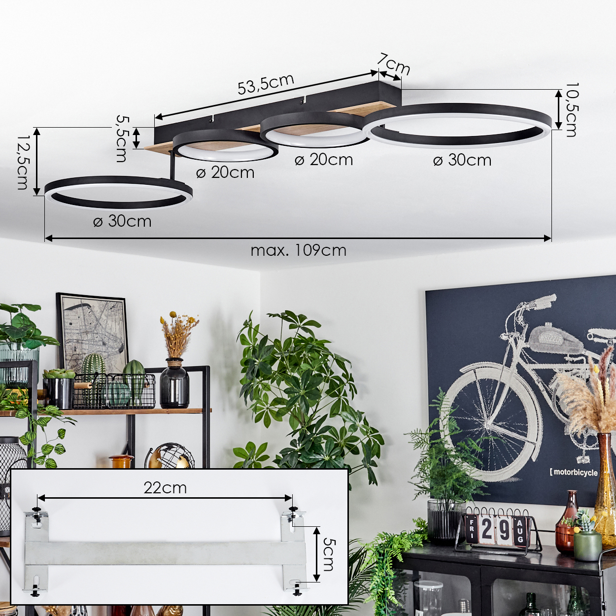 Deckenlampe mit drei Ringen und Abmessungen, mit Halterungsskizze, vor weißer Decke und Wohnraum.
