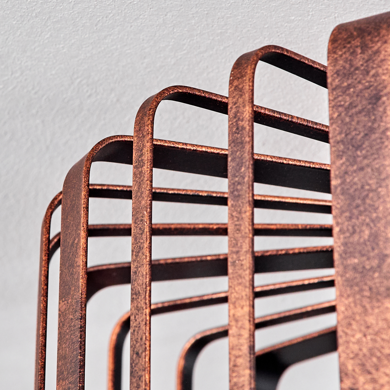 Nahaufnahme einer bronzefarbenen, käfigartigen Deckenleuchte. Die Metallstäbe sind gebogen und erzeugen ein Muster.