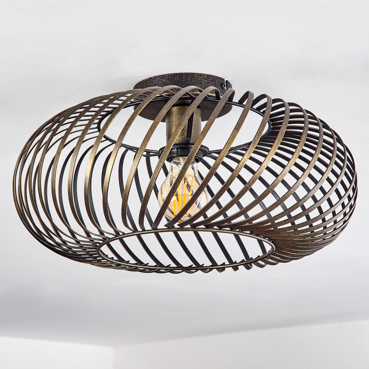 Eine bronzefarbene, spiralförmige Deckenlampe hängt von der Decke, mit einer sichtbaren Glühbirne in der Mitte.