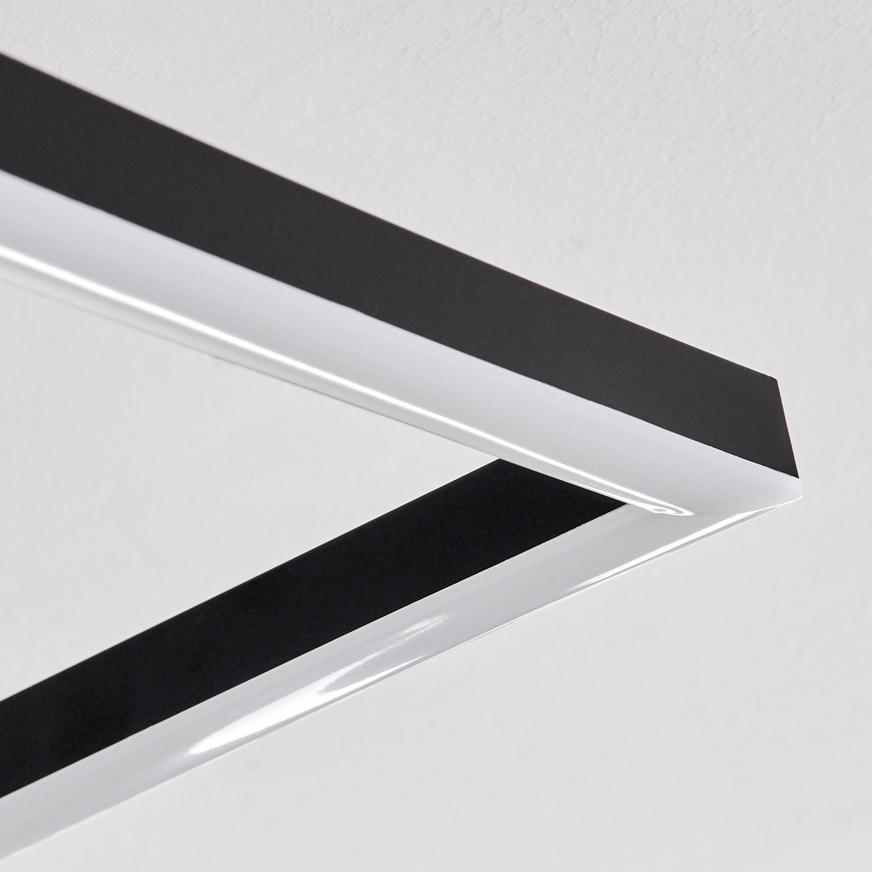 Nahaufnahme einer modernen Deckenlampe mit schwarz-weißen geometrischen Formen, die einen quadratischen Rahmen bilden.