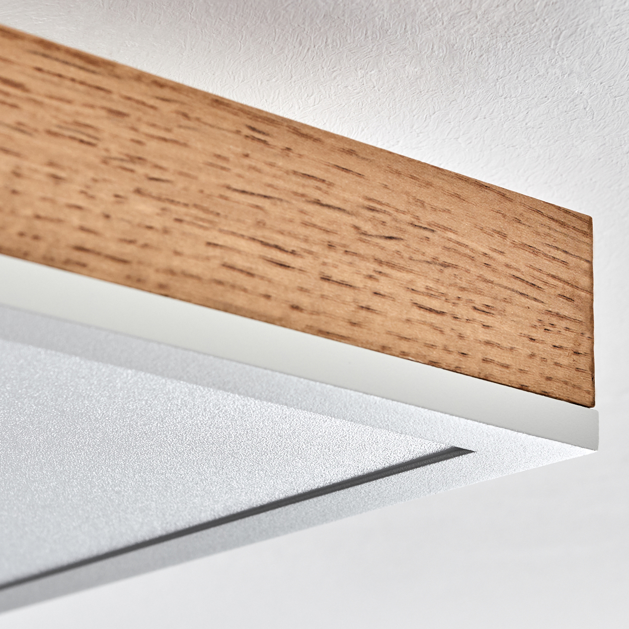 Nahaufnahme eines Holzbalkens, der an einer weißen Decke befestigt ist. Die Holzmaserung ist sichtbar, darunter ein weißer Metallstreifen.
