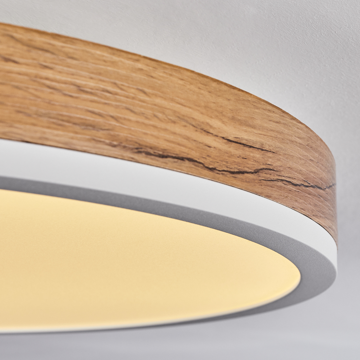 Nahaufnahme einer runden Deckenlampe mit Holzverkleidung und weißem Innenkreis, die warmes Licht aussendet.