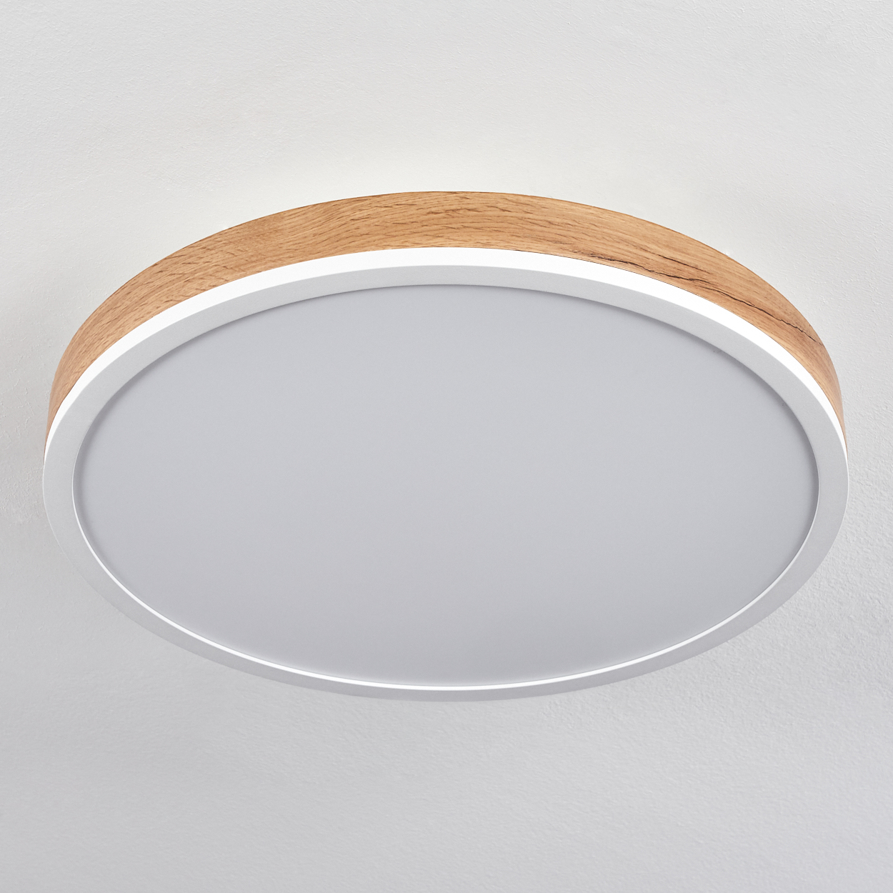 Runde Deckenlampe mit Holzmaserung und weißer Mitte, an einer weißen Decke.