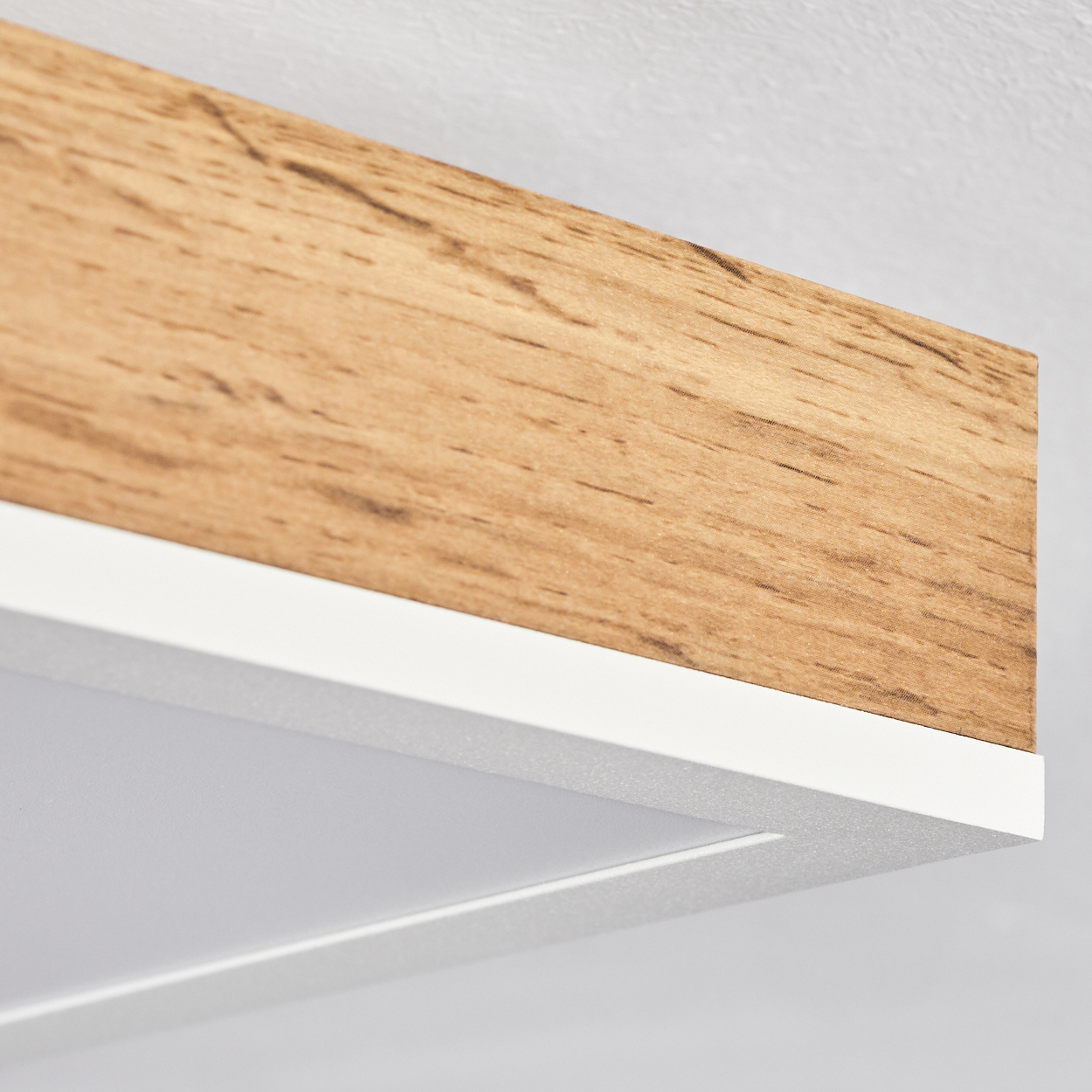 Nahaufnahme einer Deckenleuchte. Holzrahmen, weiße Zierleisten und ein weißes Lichtpaneel sind sichtbar.