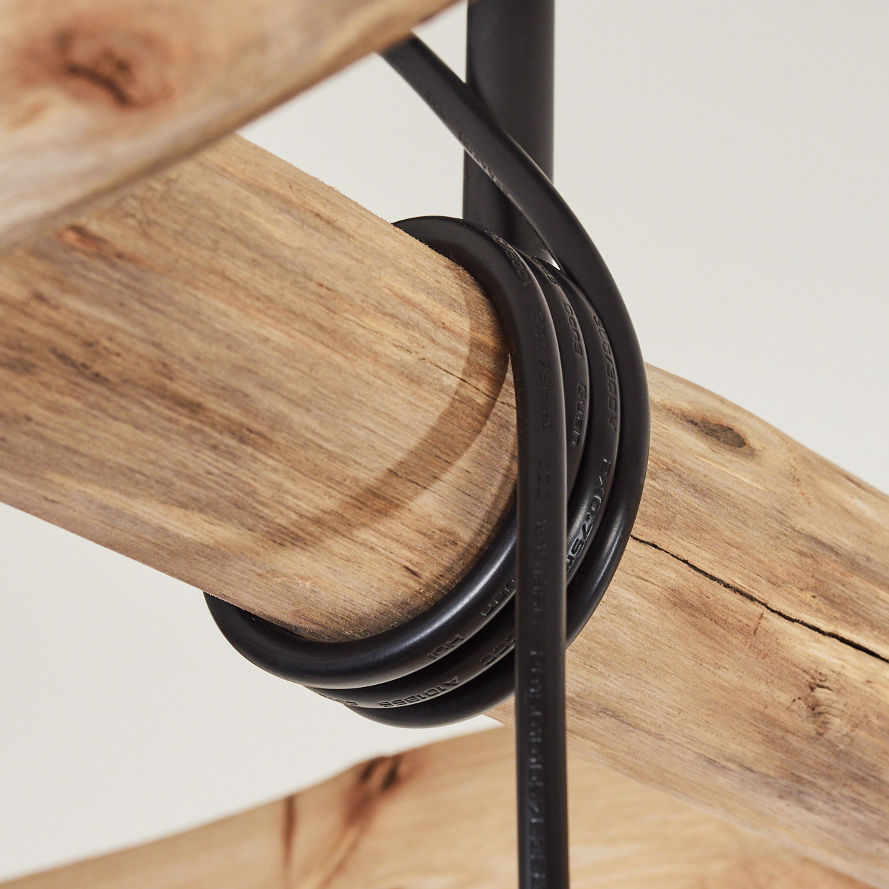 Nahaufnahme eines Holzbalkens mit einem schwarzen Kabel, das darum gewickelt ist, natürliches Licht.