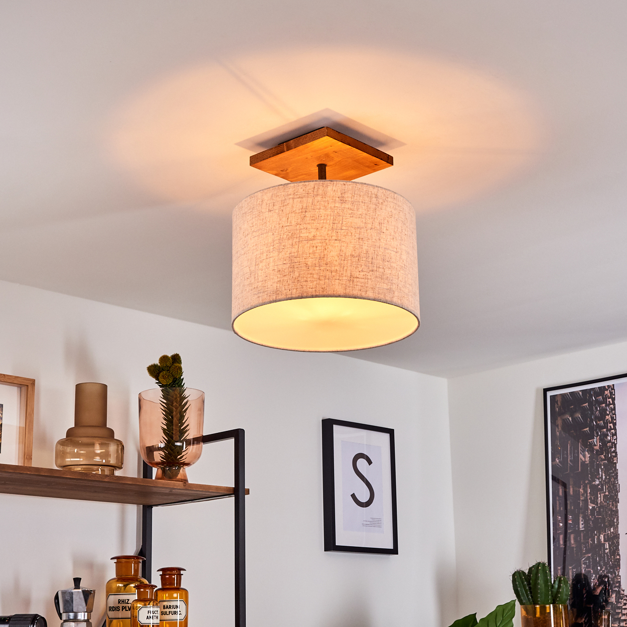 Deckenlampe mit quadratischer Holzbasis, beigem Trommelschirm und warmem Licht, mit Raumhintergrund.