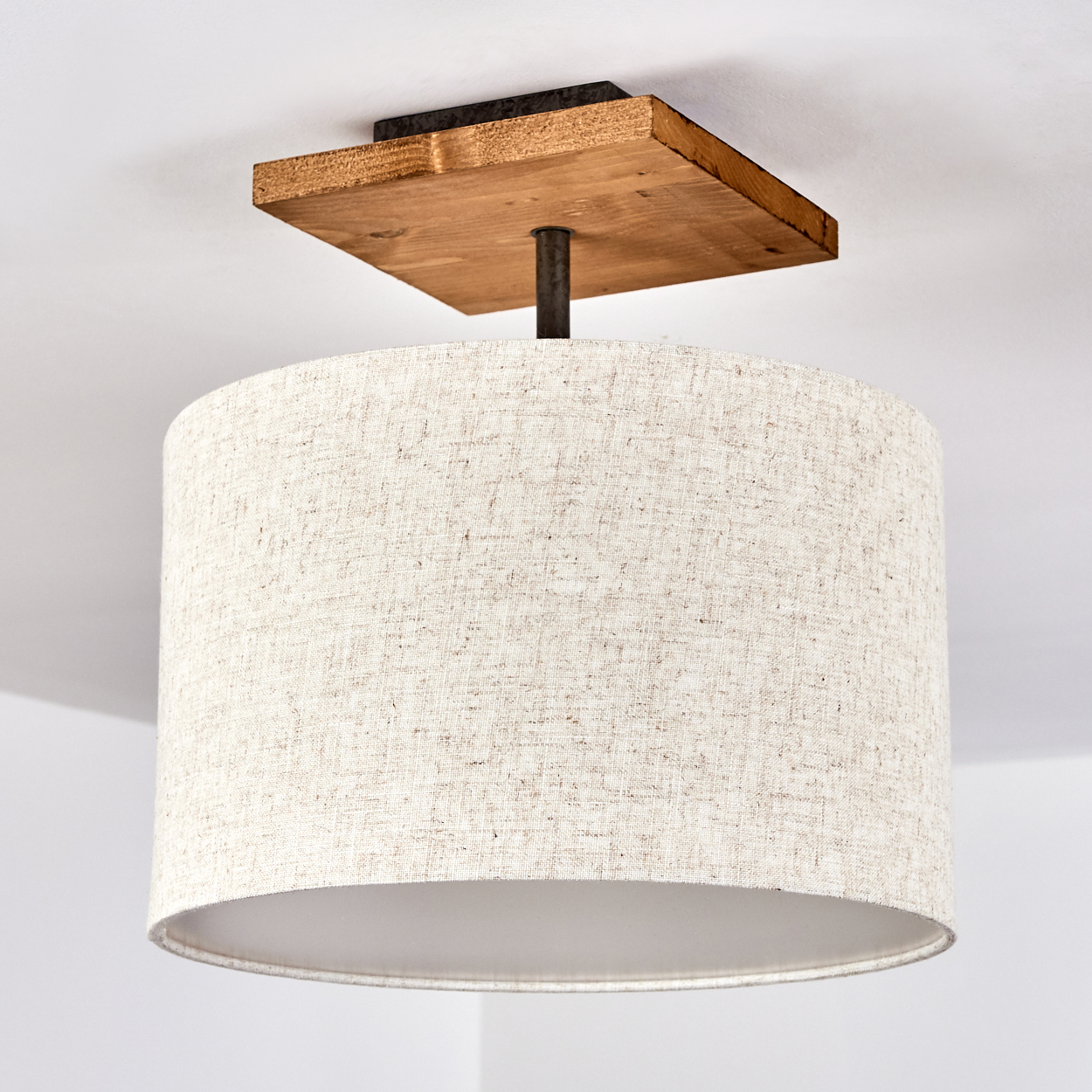 Deckenlampe mit quadratischer Holzbasis, beigem Trommelschirm und weißem Deckenhintergrund.