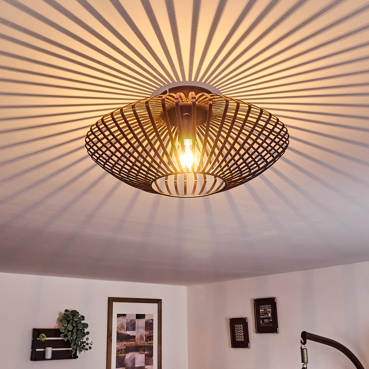 Bronzefarbene Käfig-Deckenleuchte, wirft ein radiales Lichtmuster an die Decke.