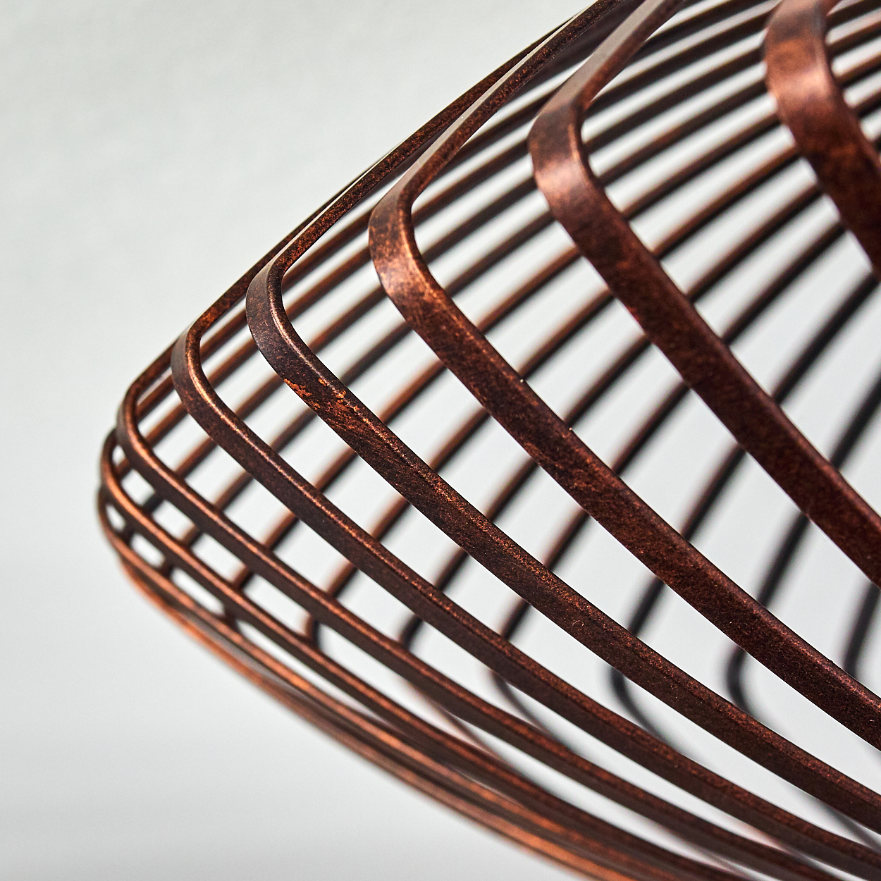 Nahaufnahme eines bronzefarbenen Metall-Lampenschirms mit Spiraldesign vor weißem Hintergrund.