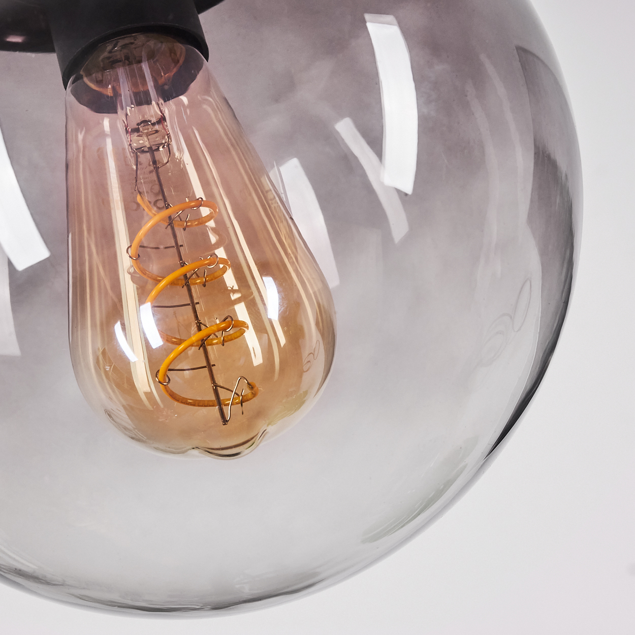 Nahaufnahme einer Glühbirne in einem rauchglasfarbenen Lampenschirm. Die Glühbirne ist orange mit einem Wendelfaden.