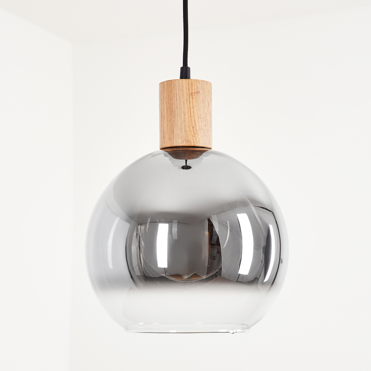 Eine einzelne Glas-Pendelleuchte mit Holzaufsatz. Der Glasteil ist reflektierend und grau.