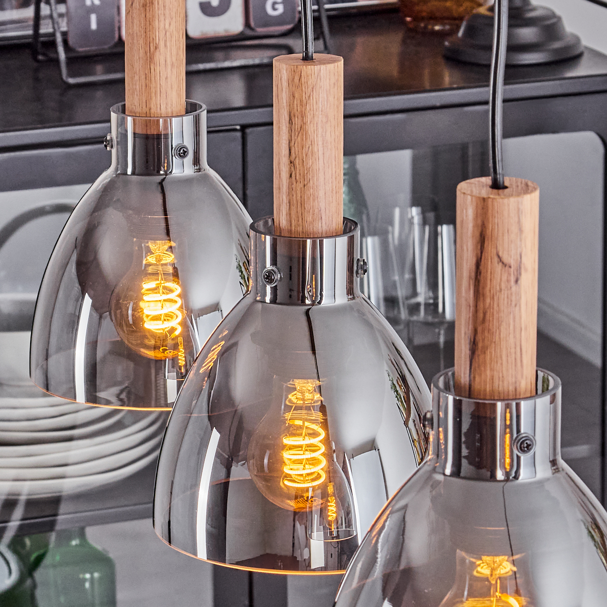 Nahaufnahme von Pendelleuchten. Drei Pendelleuchten mit Glasschirmen und Holzaufsätzen vor dunklem Hintergrund.