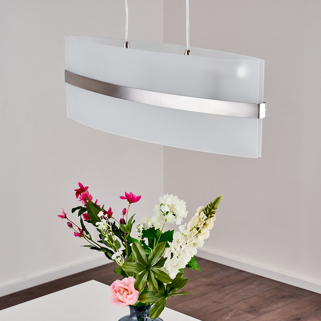 Weiße Deckenlampe über einem Tisch mit Blumen in einer dunklen Vase. Die Lampe ist eingeschaltet.