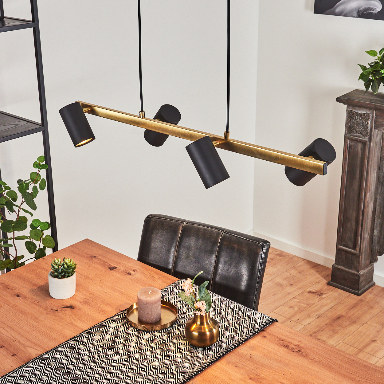 Ein Esszimmer mit einem Holztisch, einem schwarzen Stuhl und einer Lampe mit Strahlern. Die Lampe ist gold und schwarz.