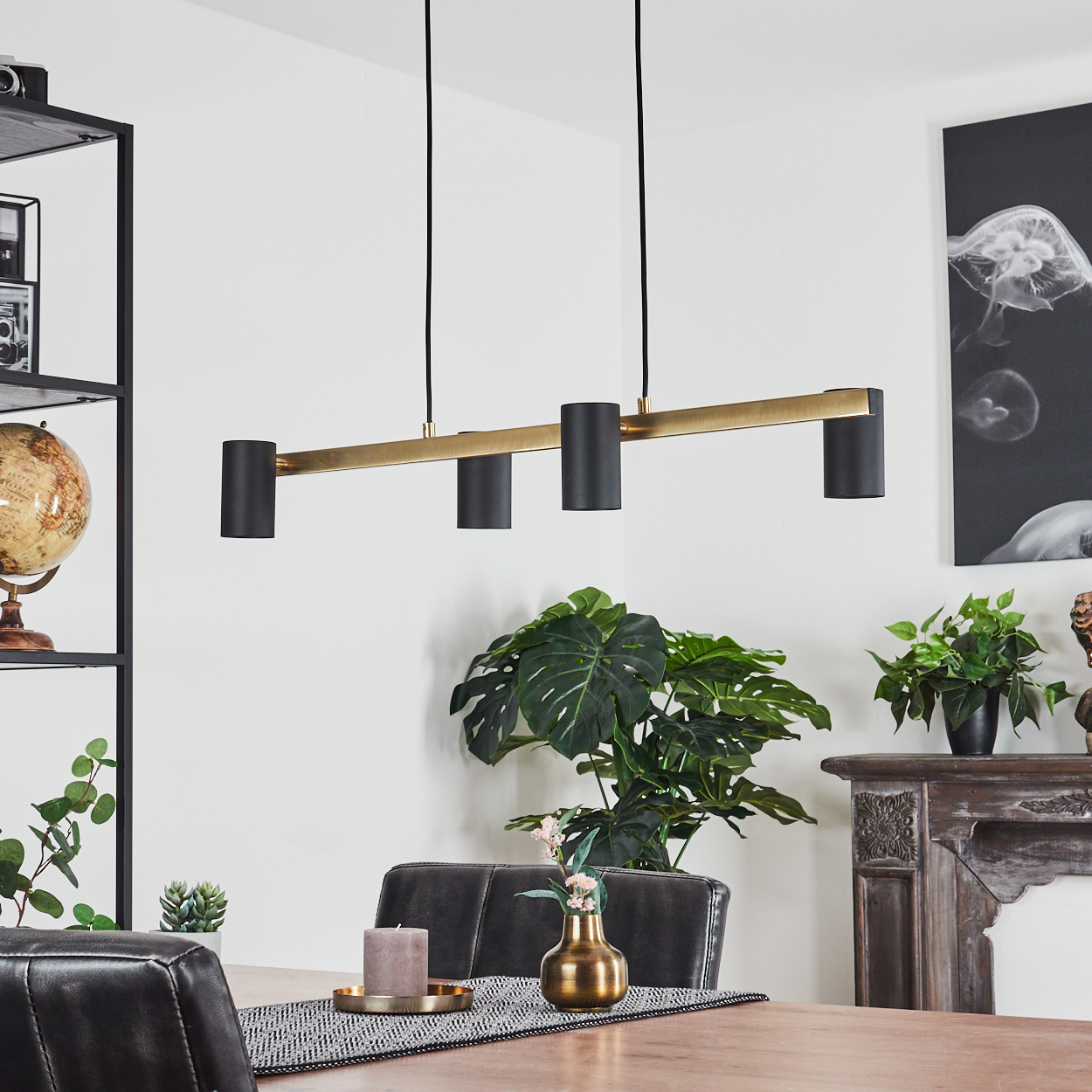 Ein Esszimmer mit einem langen Holztisch. Darüber hängt eine schwarz-goldene Leuchte. Pflanzen und Dekoration sind vorhanden.