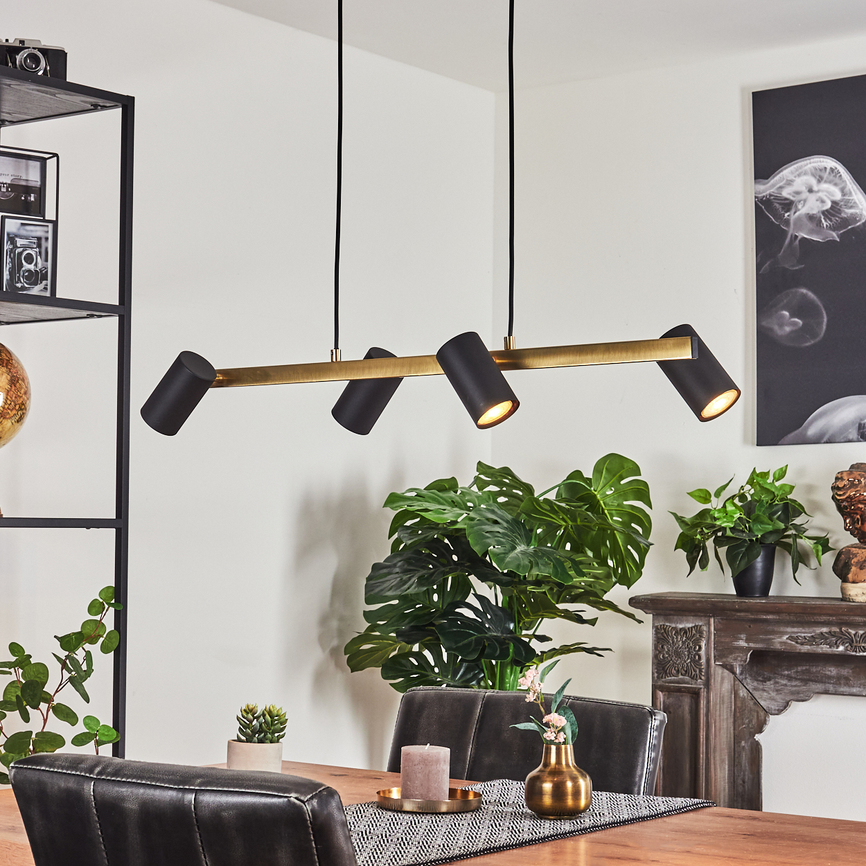 Esszimmer mit einer schwarz-goldenen Leuchte. Das Licht ist an. Vier schwarze Leuchten an einer goldenen Stange. Die Lichter sind abgewinkelt.