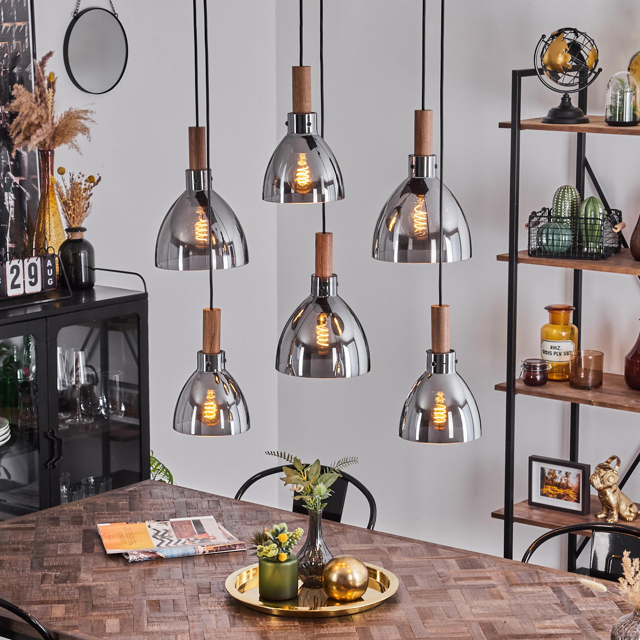 Ein Esszimmer mit sechs Pendelleuchten. Die Lampen haben silberne Schirme, Holzakzente und hängen über einem Tisch.