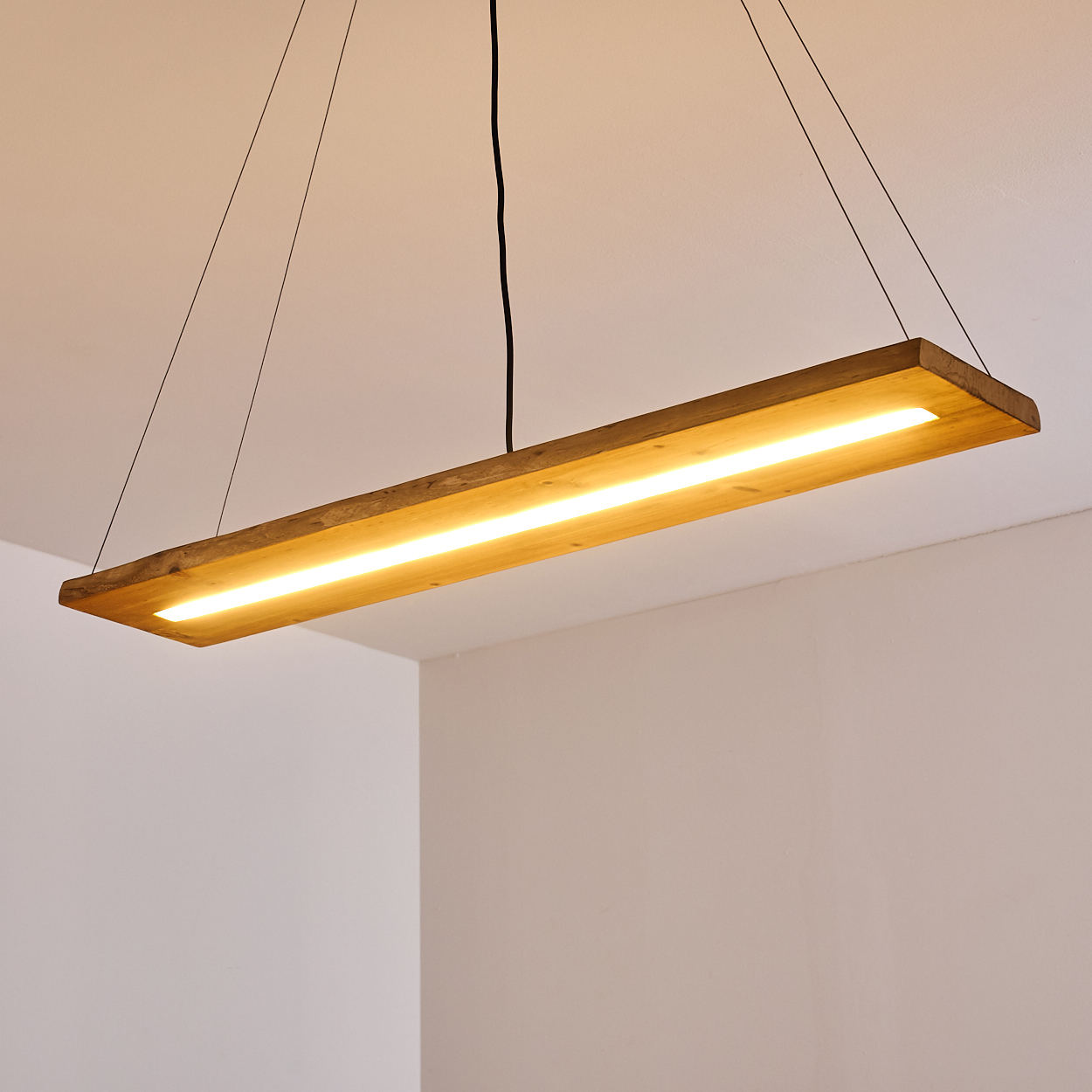 Eine rechteckige Holzbalken-Deckenleuchte mit zentralem LED-Lichtstreifen. Hängt von der Decke.