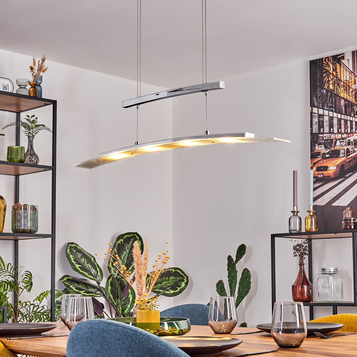 Esszimmer mit einer modernen silbernen Pendelleuchte und einem Tischgedeck. Der Raum verfügt über Pflanzen und Kunstwerke an der Wand.