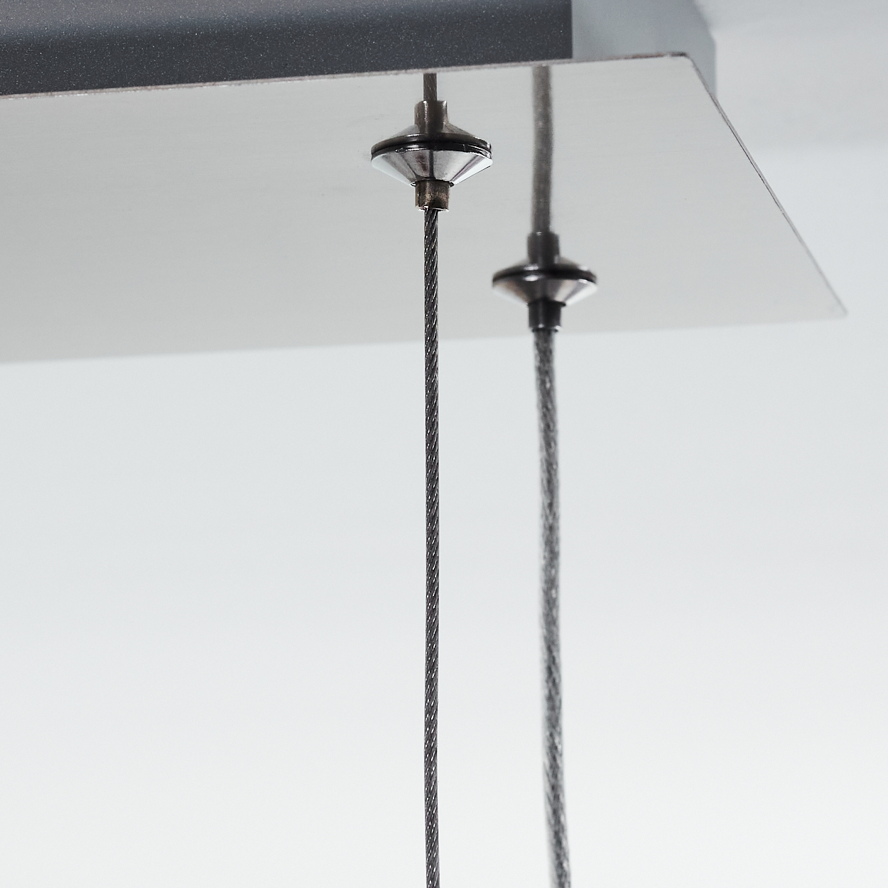 Nahaufnahme einer Deckenleuchte mit zwei herunterhängenden Drähten. Die Leuchte ist metallisch, vor einer weißen Decke.