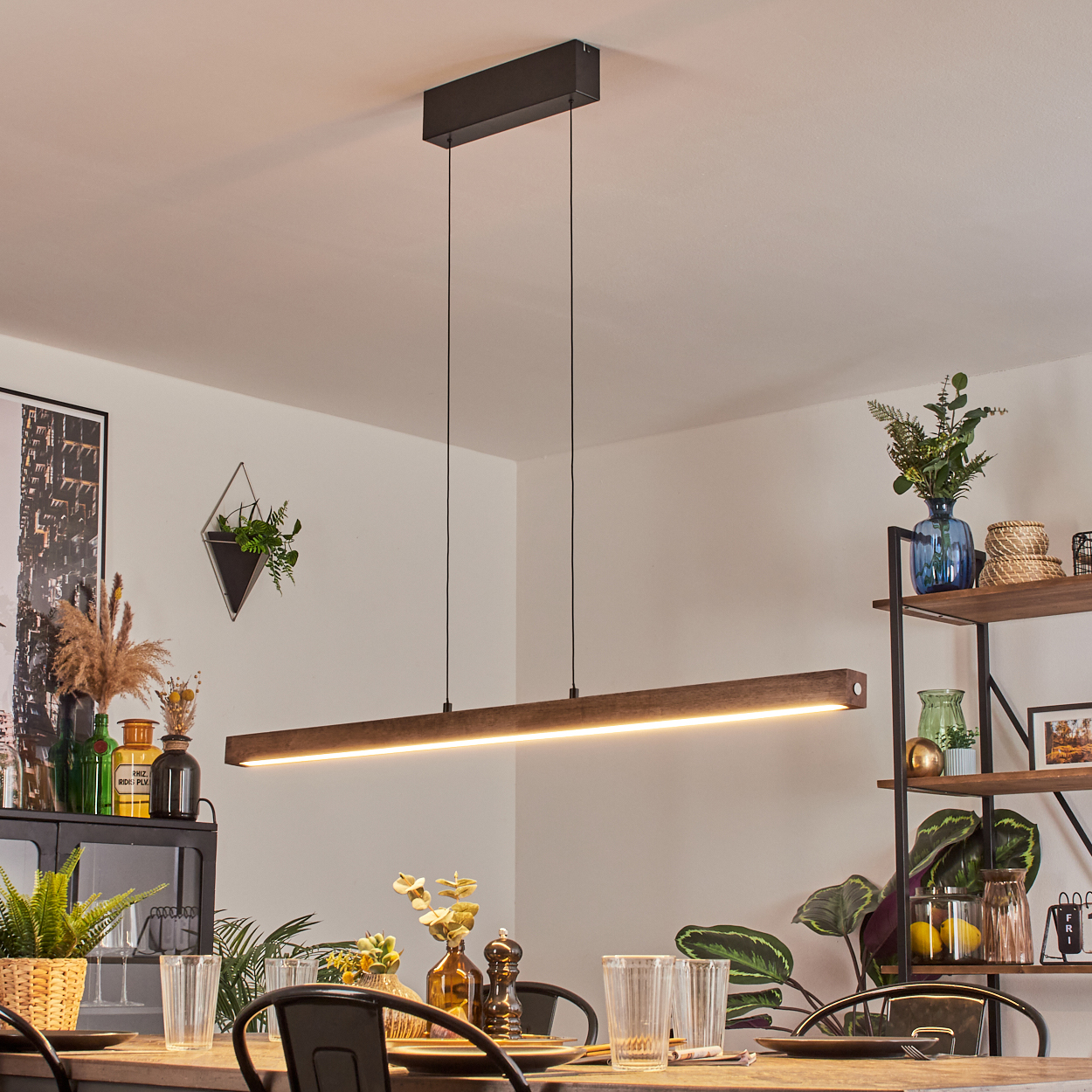 Moderne lineare LED-Leuchte. Sie hängt von der Decke. Ein Esstisch und Dekoration sind im Hintergrund.