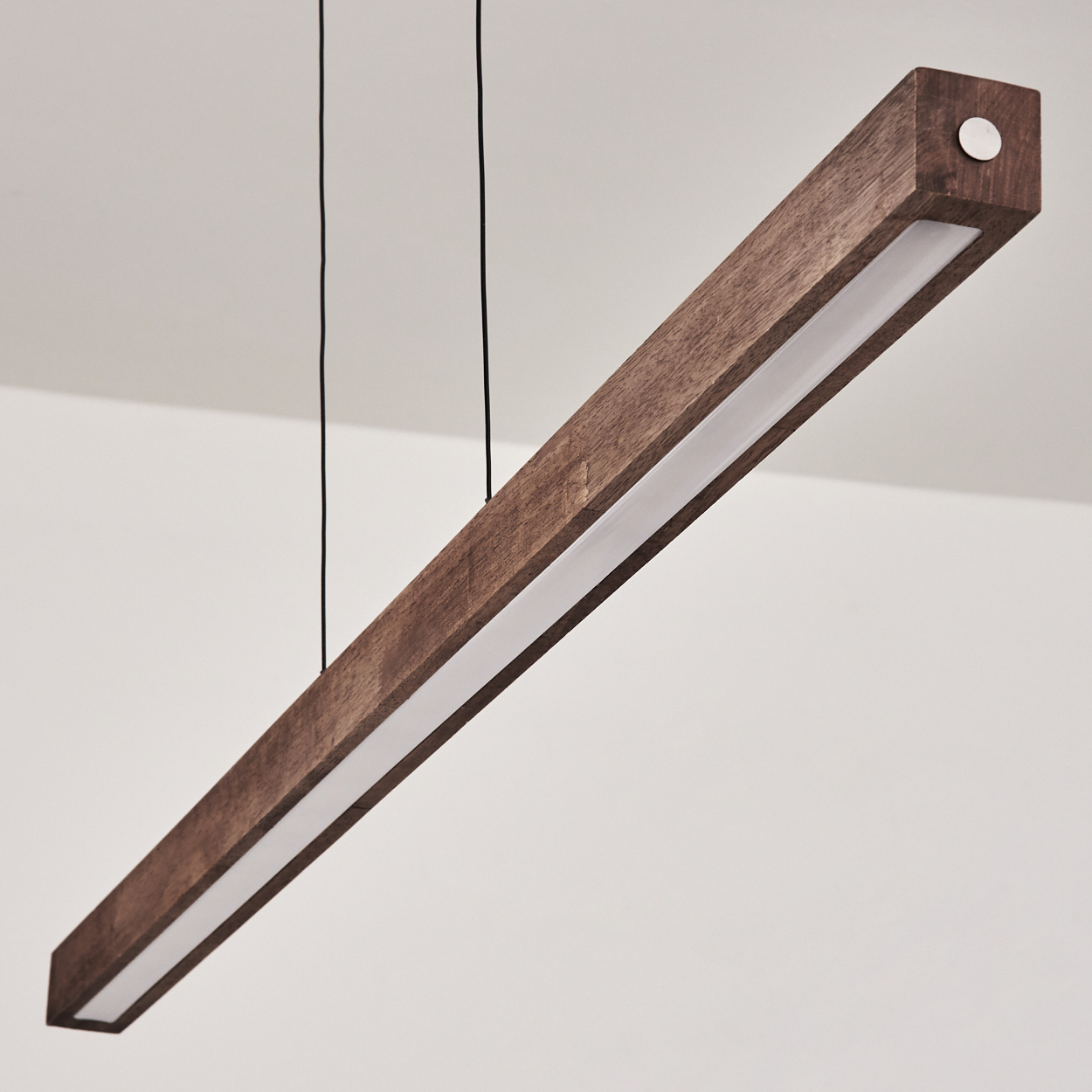 Eine rechteckige Pendelleuchte aus Holz mit weißem Lichtstreifen. Hängt an zwei dünnen schwarzen Drähten.