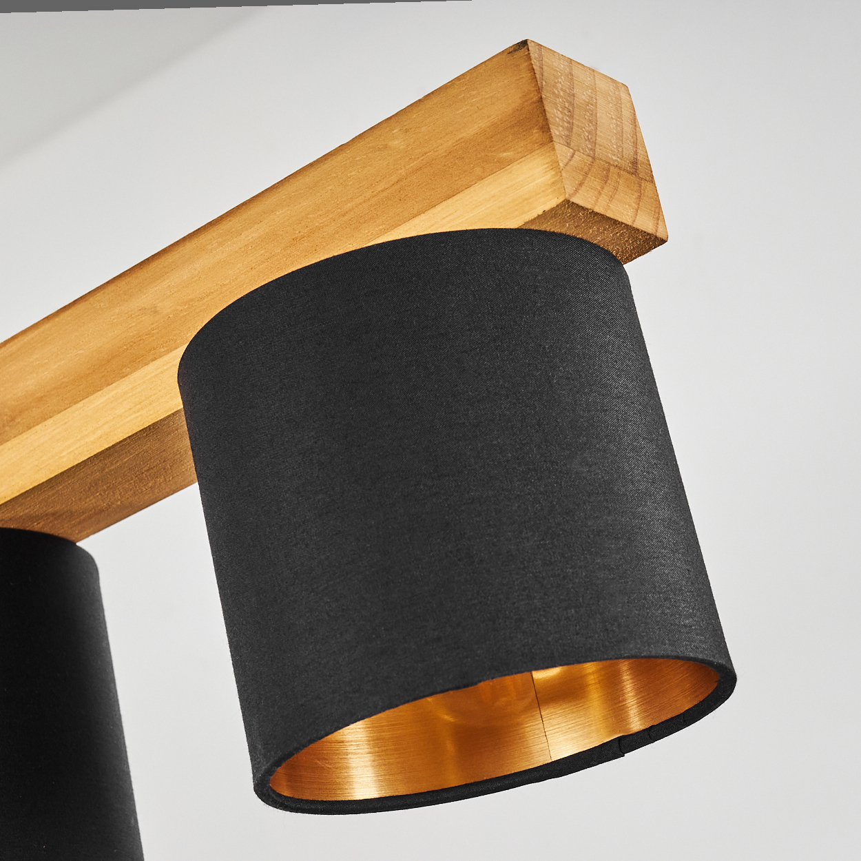 Holzbalken mit zwei schwarzen Lampenschirmen. Die Lampenschirme haben goldene Innenseiten.