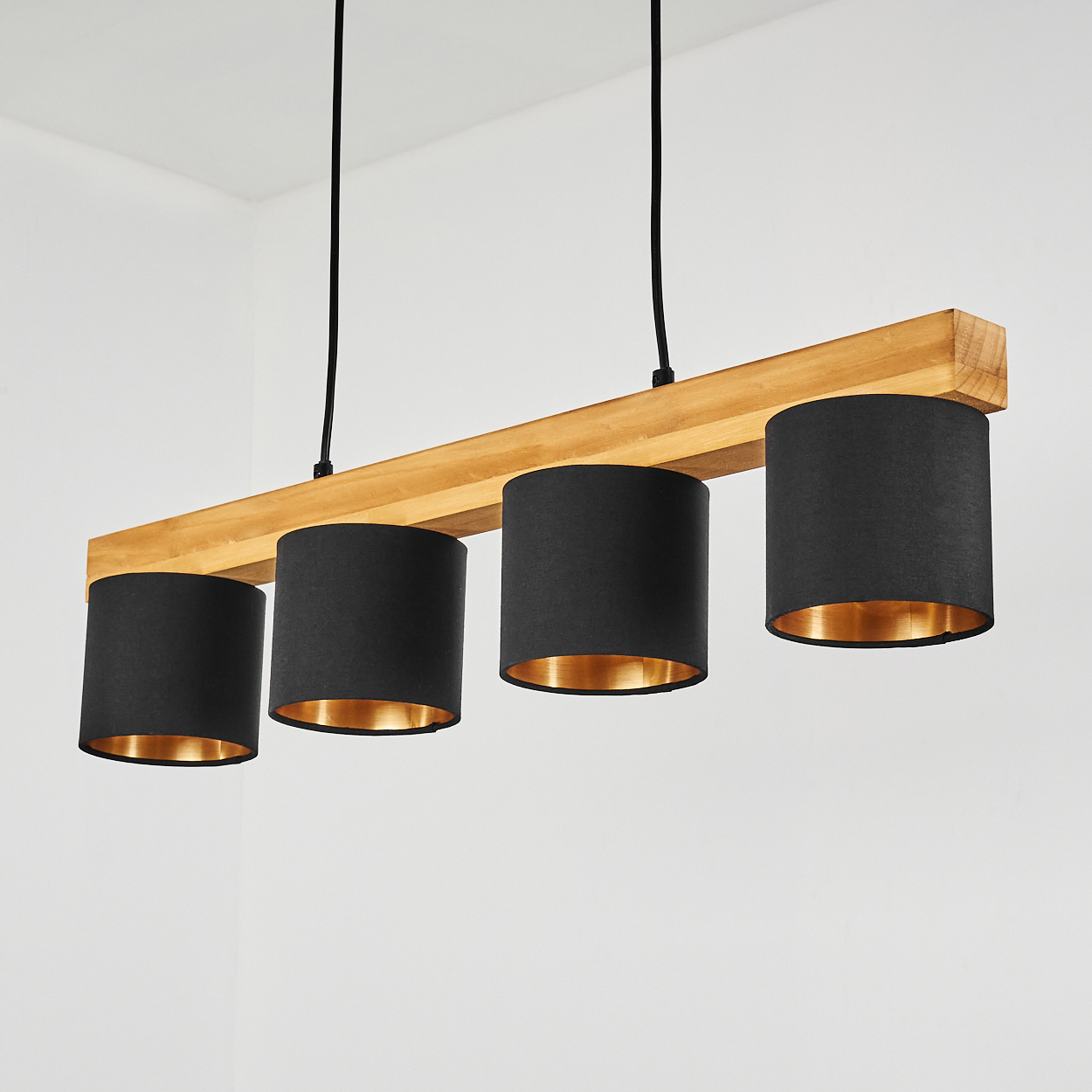 Ein Holzbalken-Kronleuchter mit vier schwarzen Lampenschirmen hängt vor einer weißen Wand.