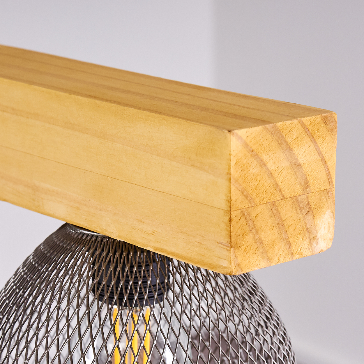 Nahaufnahme einer Holzbalken-Leuchte mit einem Drahtgeflecht-Lampenschirm und einer Glühbirne.