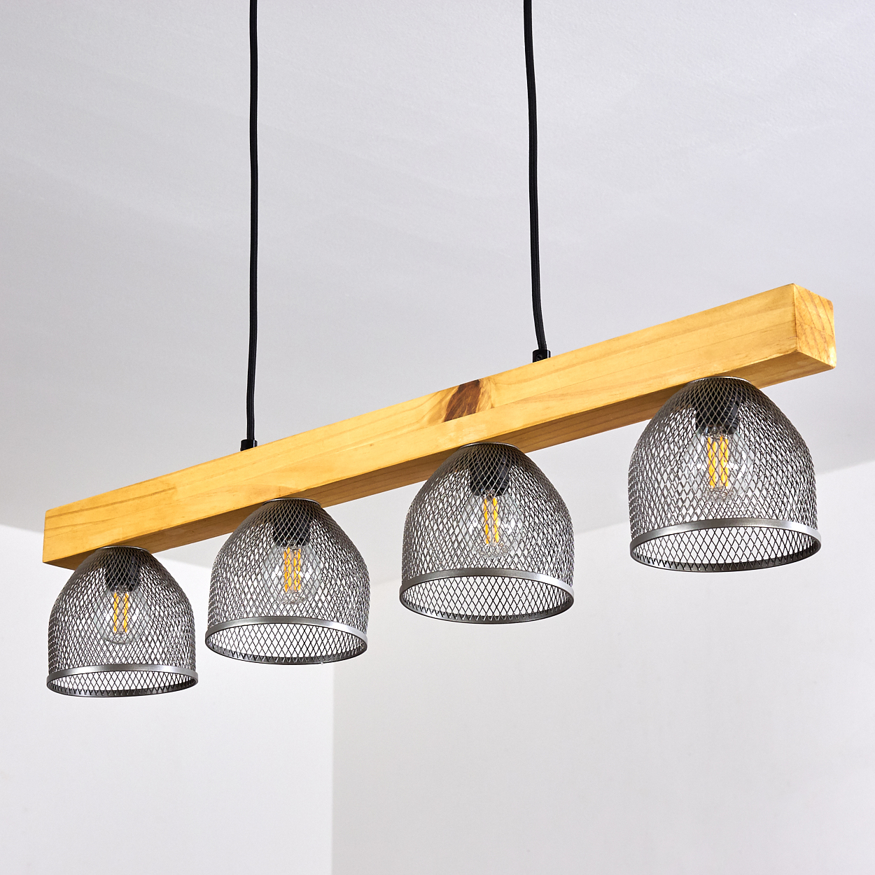 Ein Holzbalken-Kronleuchter mit vier Drahtgitter-Schirmen hängt von der Decke, vor weißem Hintergrund.