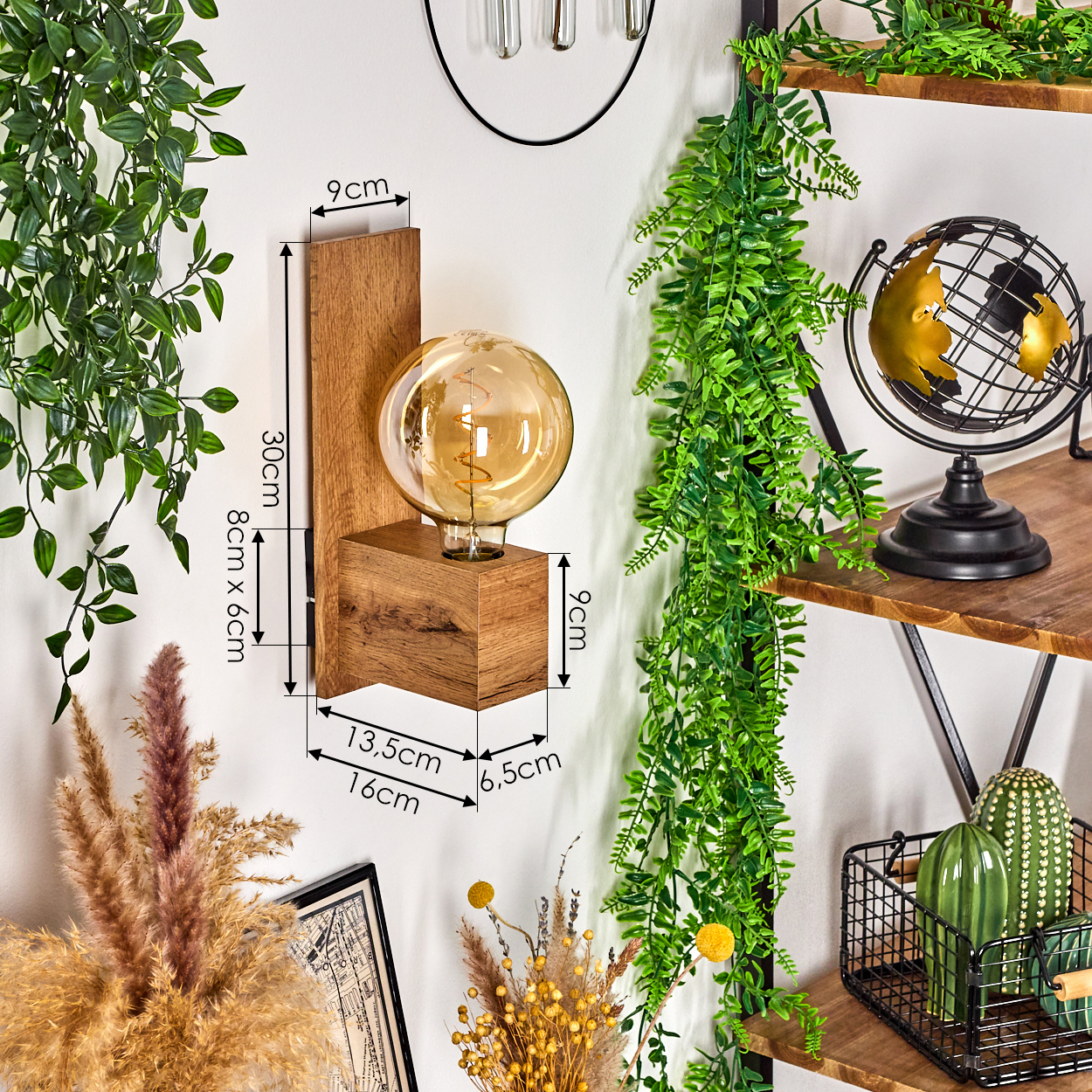 Wandlampe mit großer Glühbirne, Holzsockel und Maßangaben. Mit grünen Pflanzen im Hintergrund.