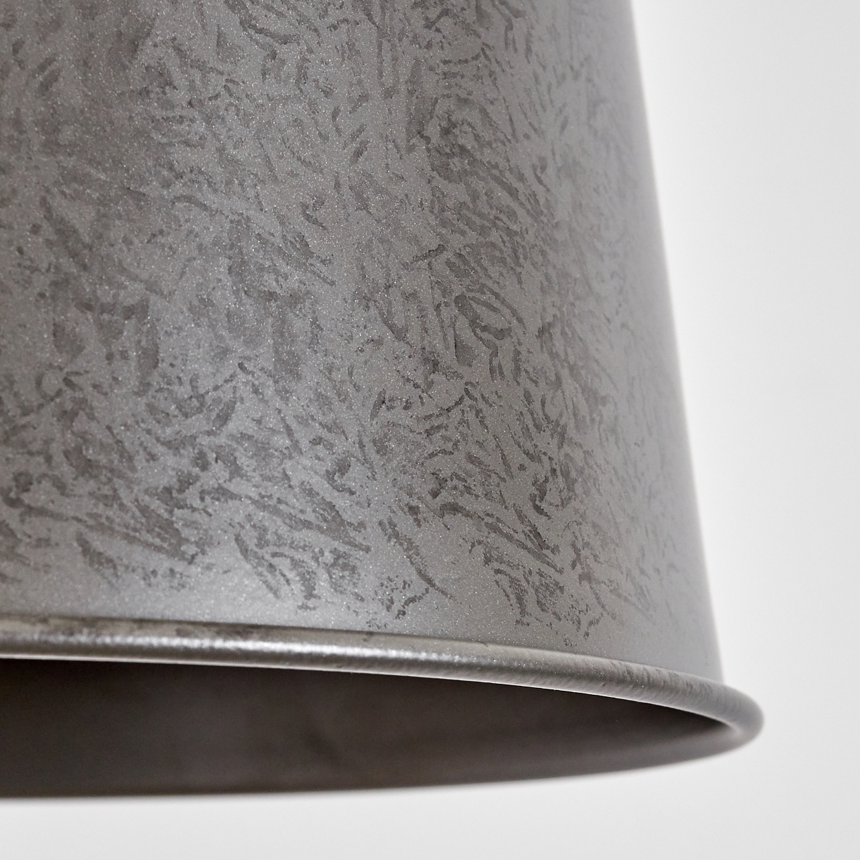 Nahaufnahme eines strukturierten, grauen Metalllampenschirms. Der Schirm ist konisch geformt und hat eine raue Oberfläche.
