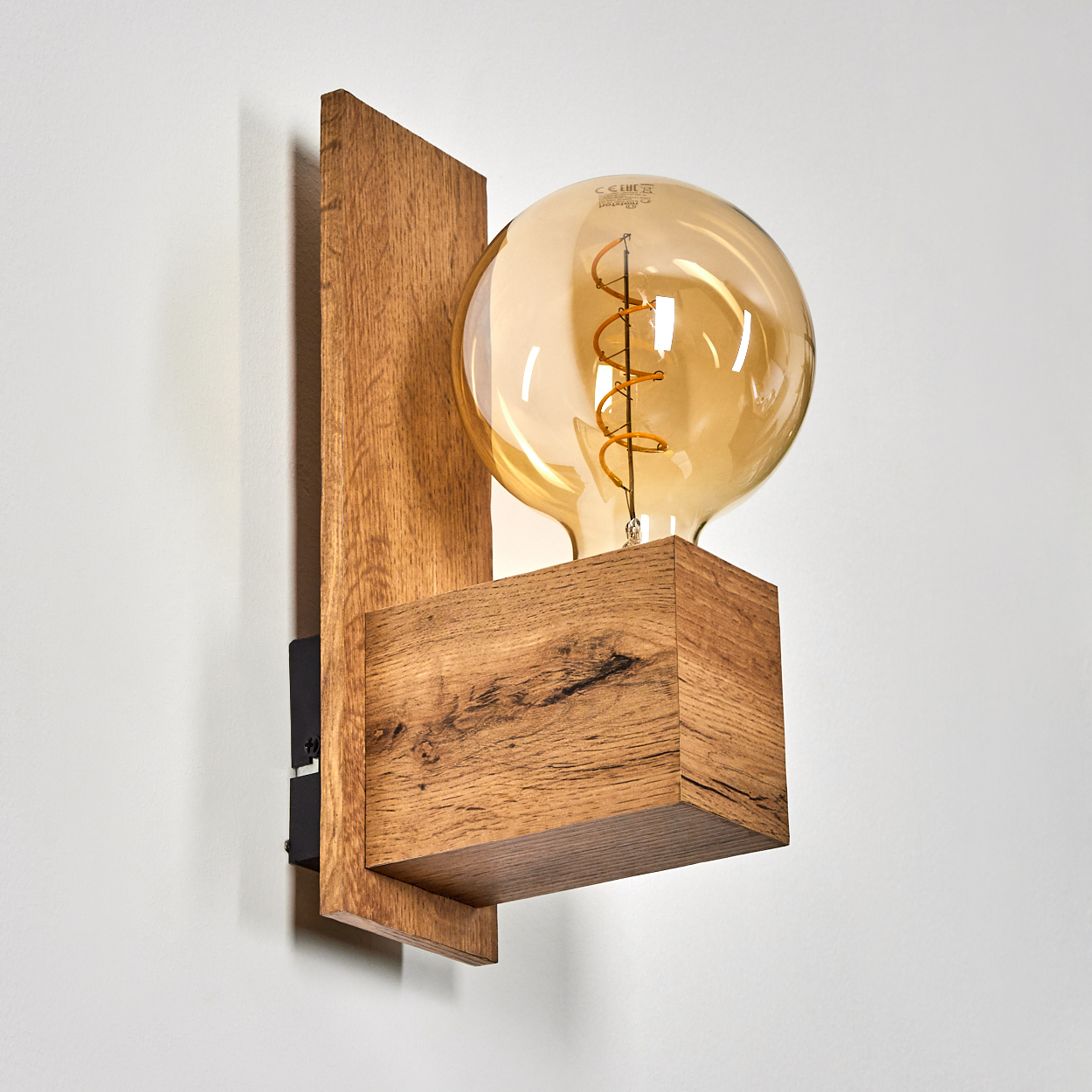 Hölzerne Wandleuchte mit einer großen Glühbirne in einem Holzblock. Die Lampe ist an einer weißen Wand mit einer schwarzen Halterung befestigt.