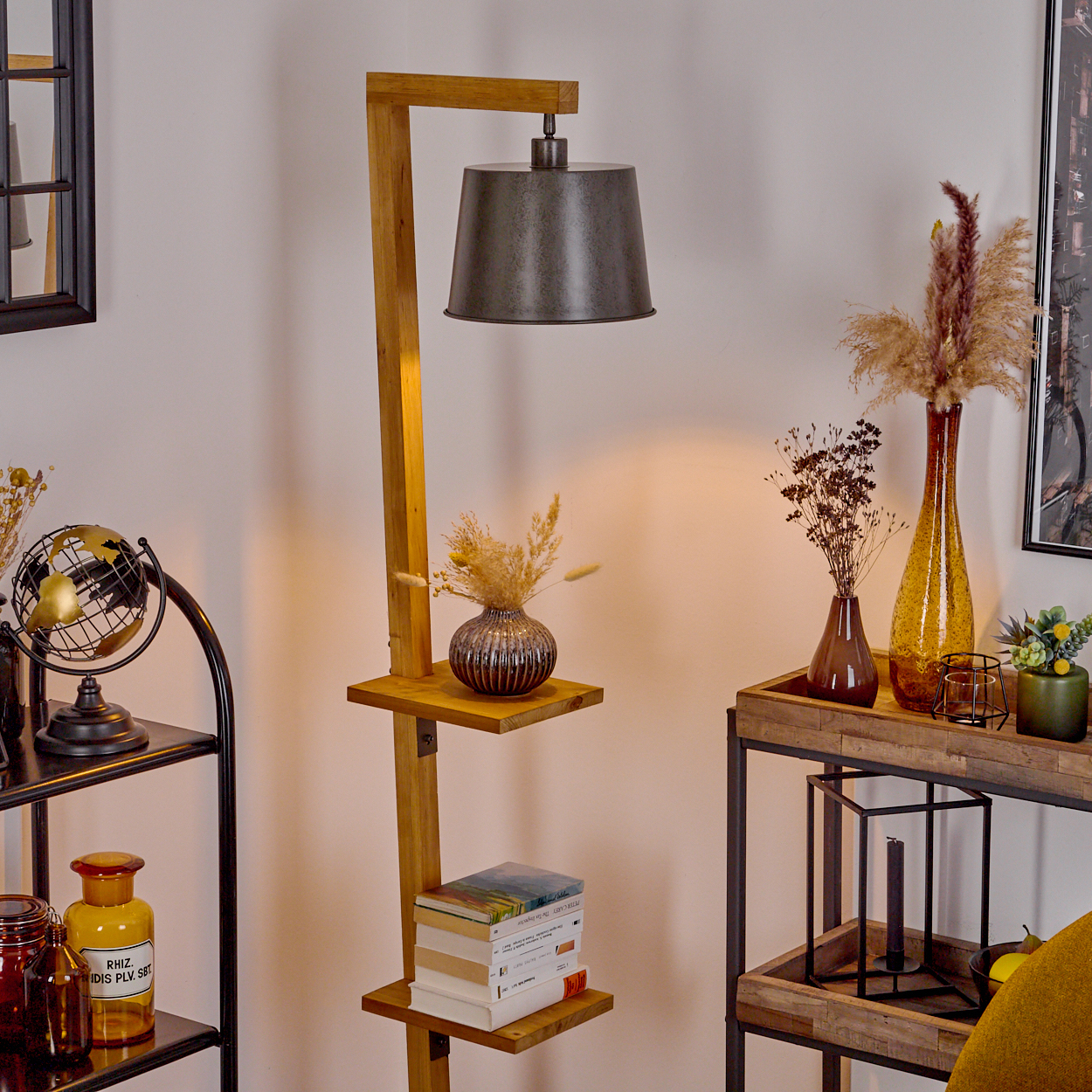 Wohnzimmer mit Stehlampe, Regalen und diverser Dekoration. Die Lampe hat einen grauen Schirm und eine Holzstruktur. Weiße Wand.