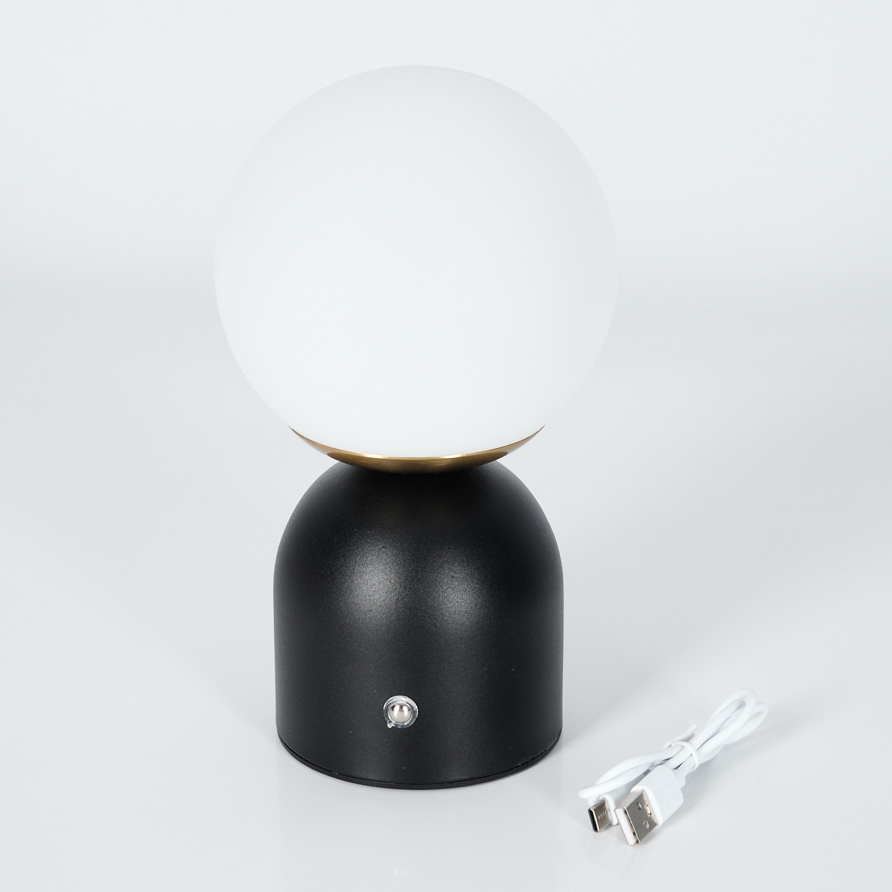 Eine schwarz-weiße Tischlampe mit runder weißer Glühbirne, daneben ein Ladekabel.