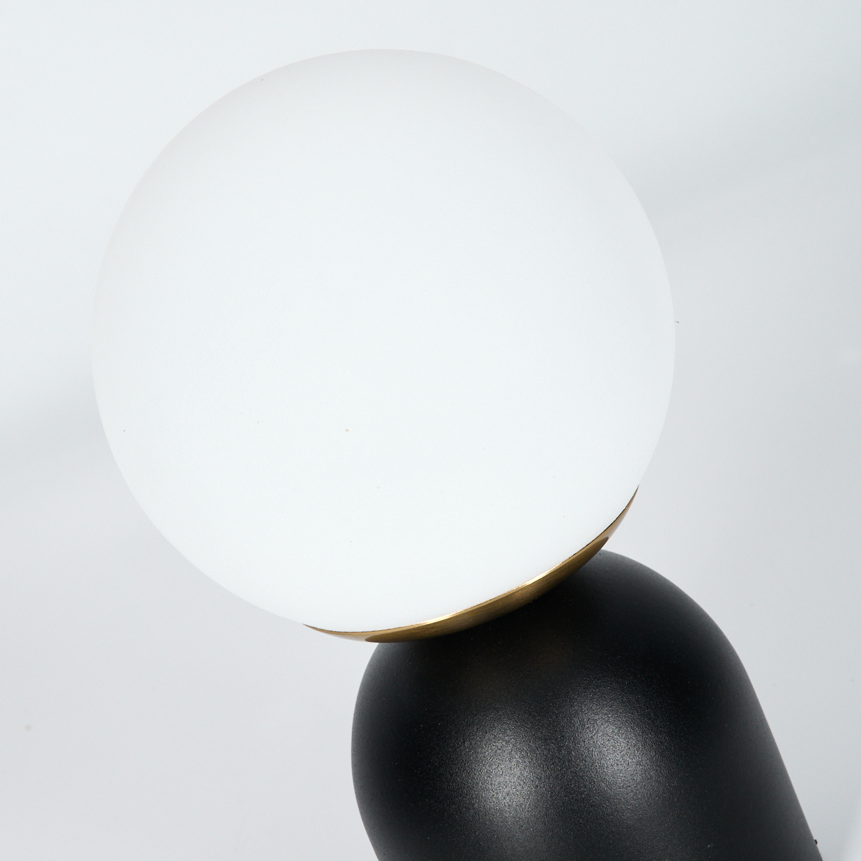 Nahaufnahme einer Lampe. Weiße Kugel, schwarzer und goldener Sockel. Weißer Hintergrund.