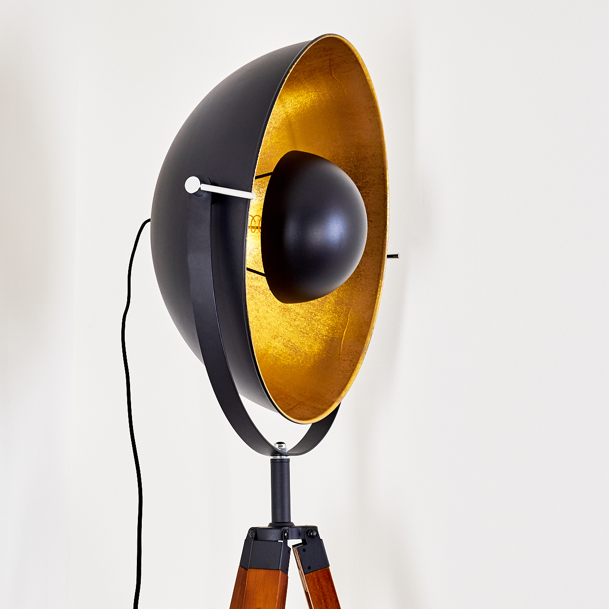 Eine schwarz-goldene Stehlampe mit kugelförmigem Schirm steht vor einer schlichten weißen Wand und zeigt ihr modernes Design.