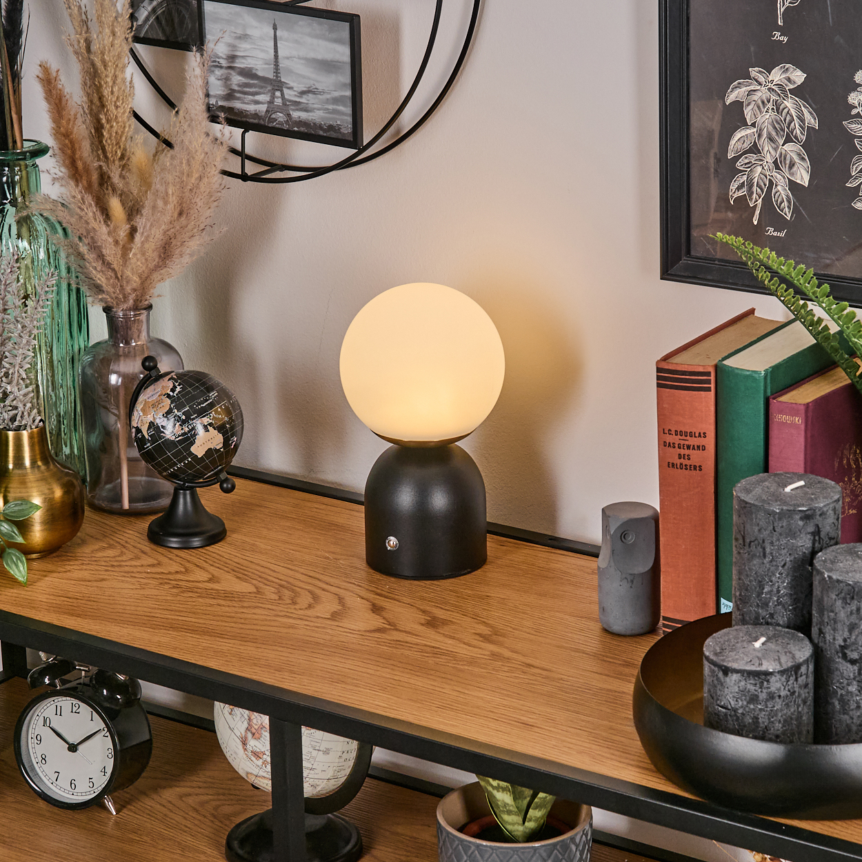 Schwarze Tischlampe mit rundem Licht, Dekorationen und Büchern auf einem Regal.