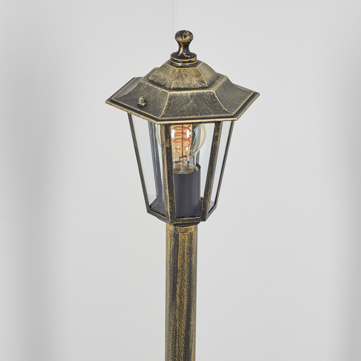 Eine Vintage-Außenlampe. Sie hat eine goldene Farbe und ist eingeschaltet. Der Hintergrund ist weiß.
