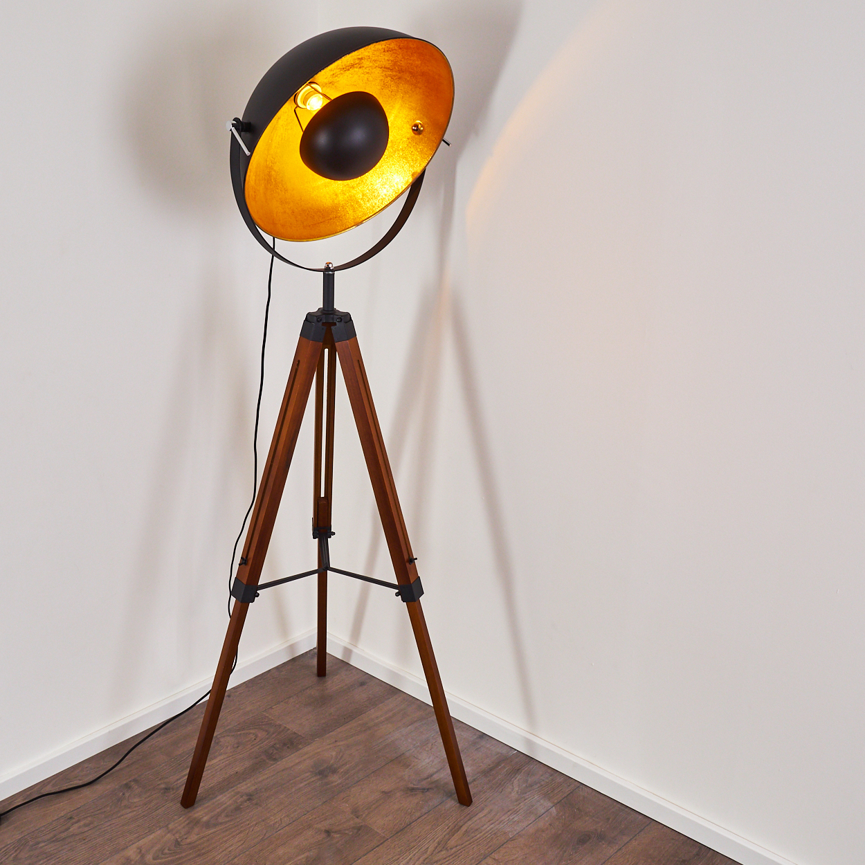Eine Stehlampe mit schwarzem Schirm und goldenem Innenraum. Die Lampe steht in einer Ecke.