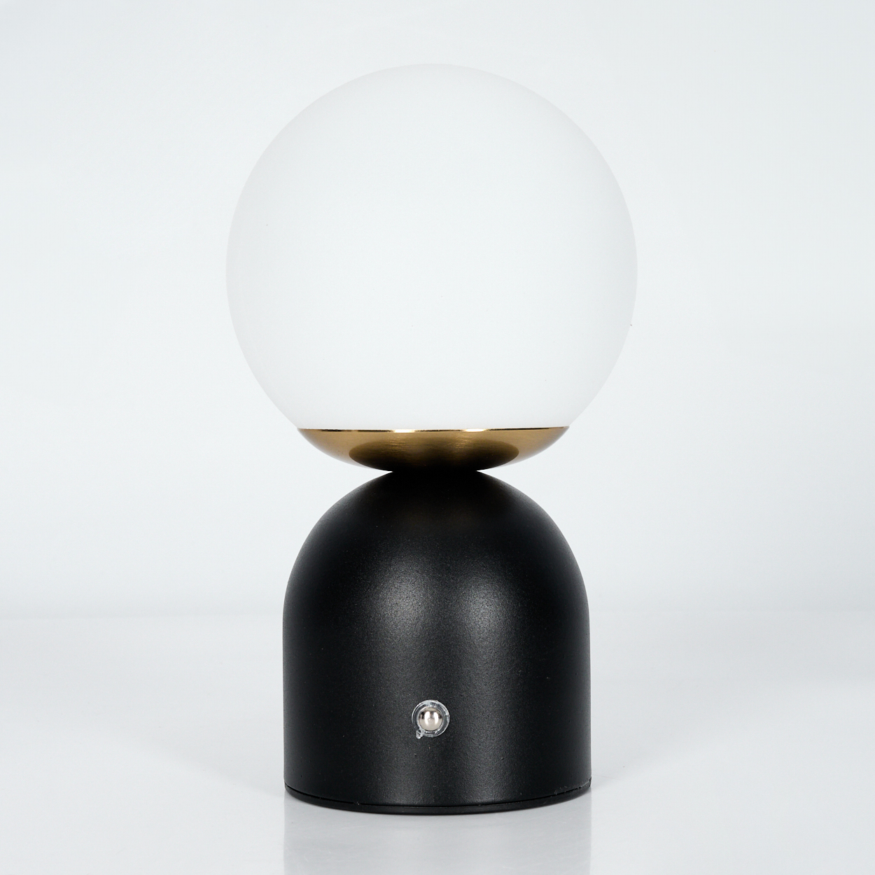 Eine schwarze Lampe mit einer weißen Kugel. Die Lampe steht auf einer weißen Oberfläche.