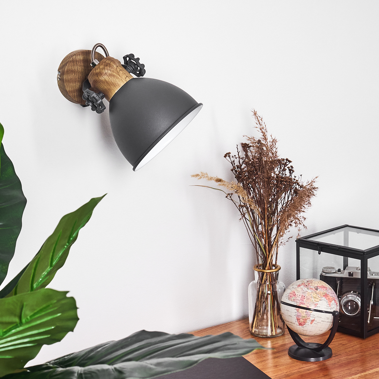 Schreibtischlampe mit grauem Schirm, Trockenblumen, Globus und Kamera auf einem Holzschreibtisch.