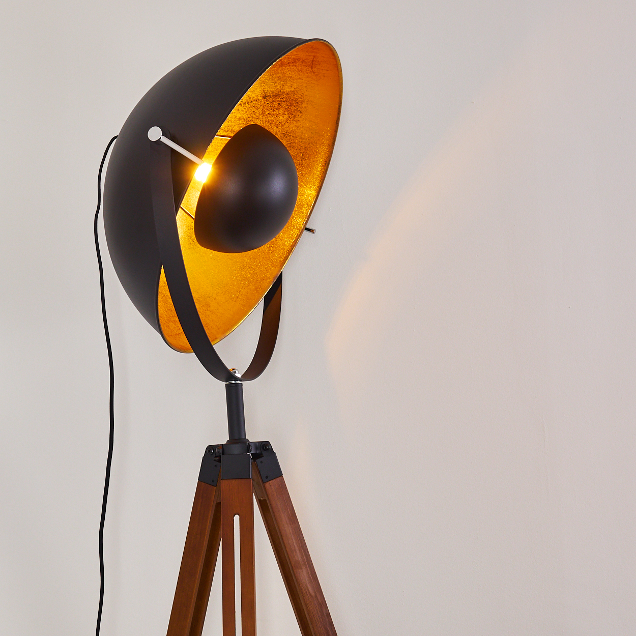 Eine Stehlampe mit schwarzem Schirm und goldenem Innenraum. Die Lampe ist eingeschaltet.