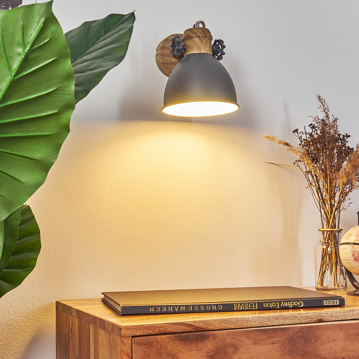 Wandlampe mit Holzsockel und schwarzem Schirm, Buch und Deko darunter.