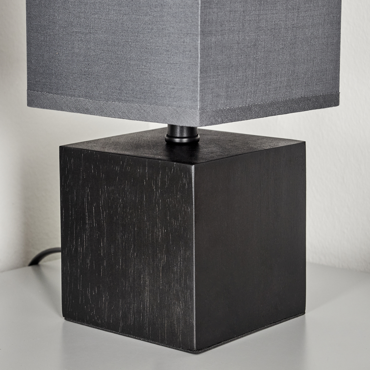Schwarze Würfellampenbasis mit grauem Lampenschirm. Die Lampe steht auf einer weißen Oberfläche.
