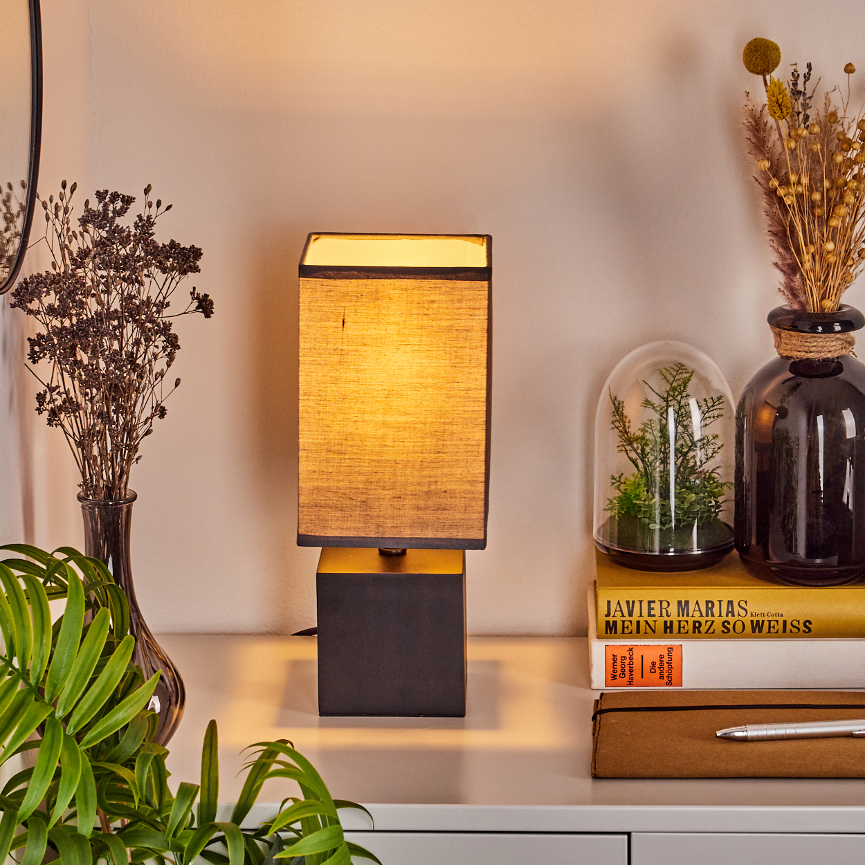 Eine Lampe mit schwarzem Sockel und Lampenschirm auf einem weißen Tisch mit Blumenvase.
