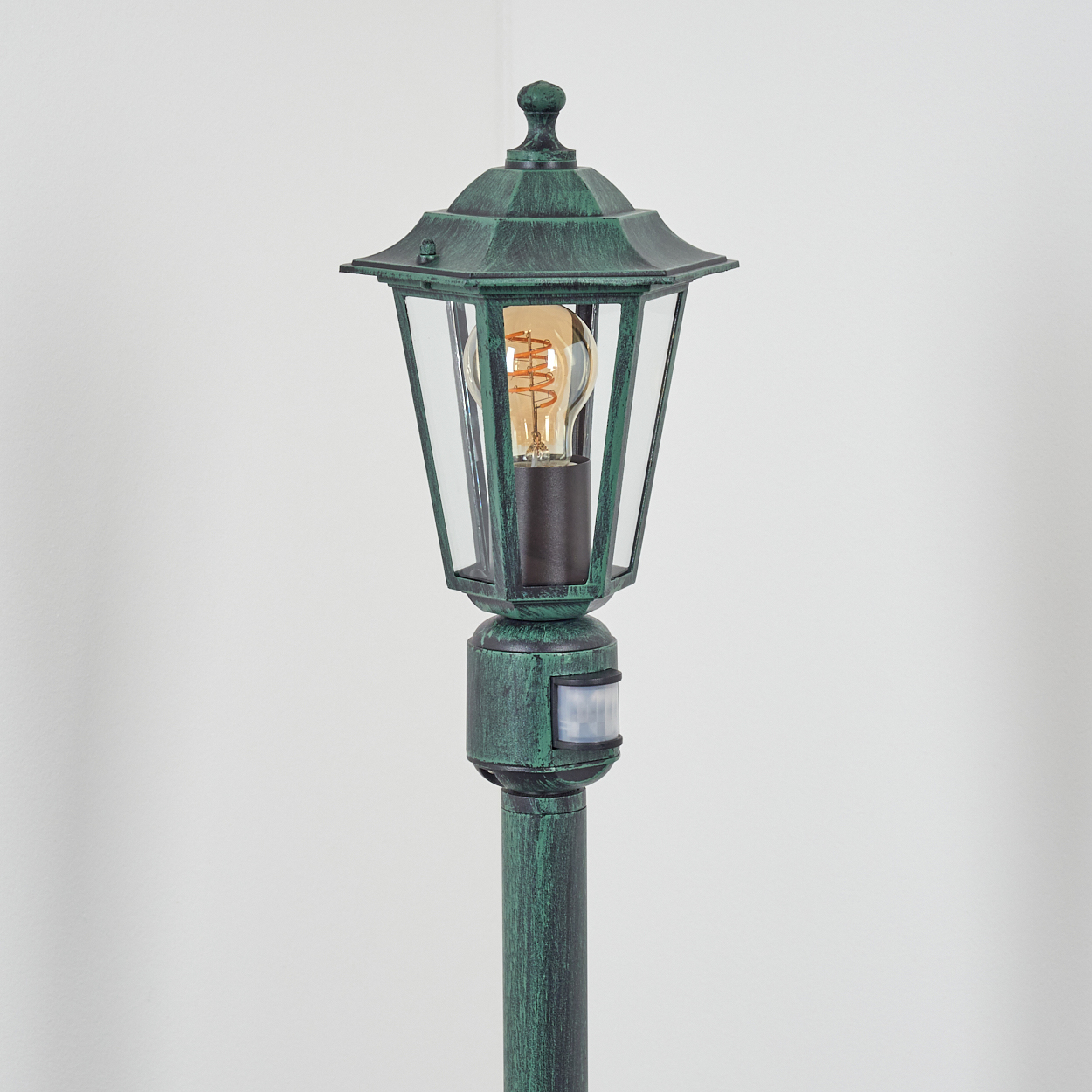Eine grüne Außenlampe mit klarer Glasabdeckung und Glühbirne im Inneren.