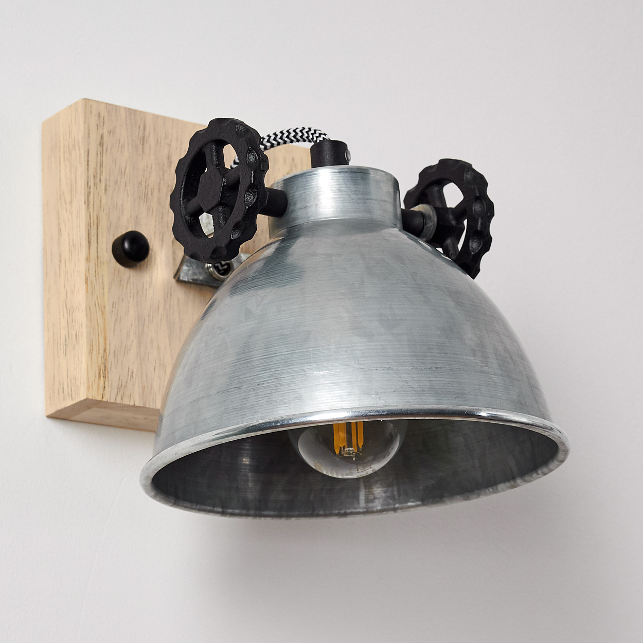 Wandmontierte Metalllampe mit Zahnradakzenten auf einem hellen Holzsockel, die ein warmes Licht ausstrahlt.
